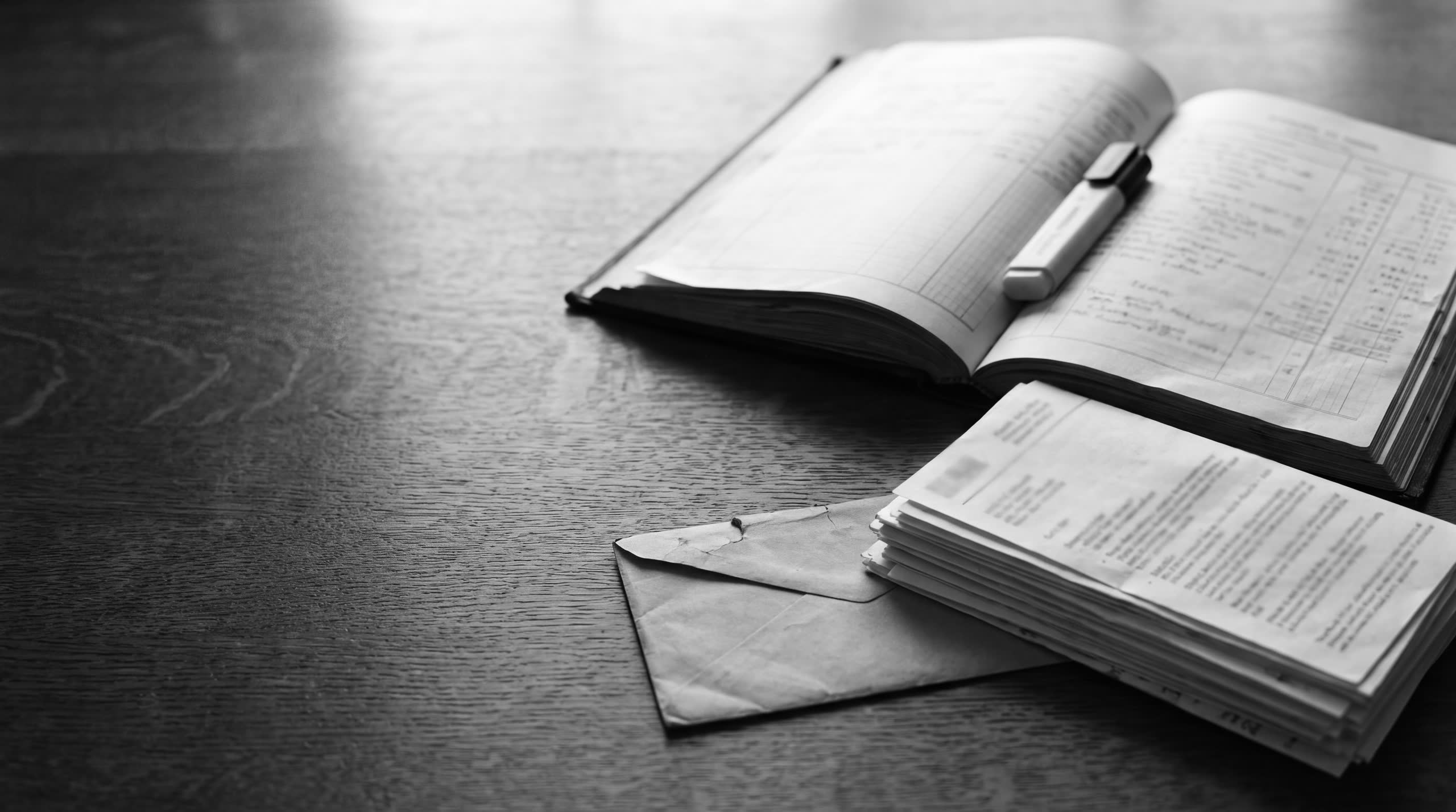 An open ledger, a highlighter, a stack of statements and an envelope on an oak desk